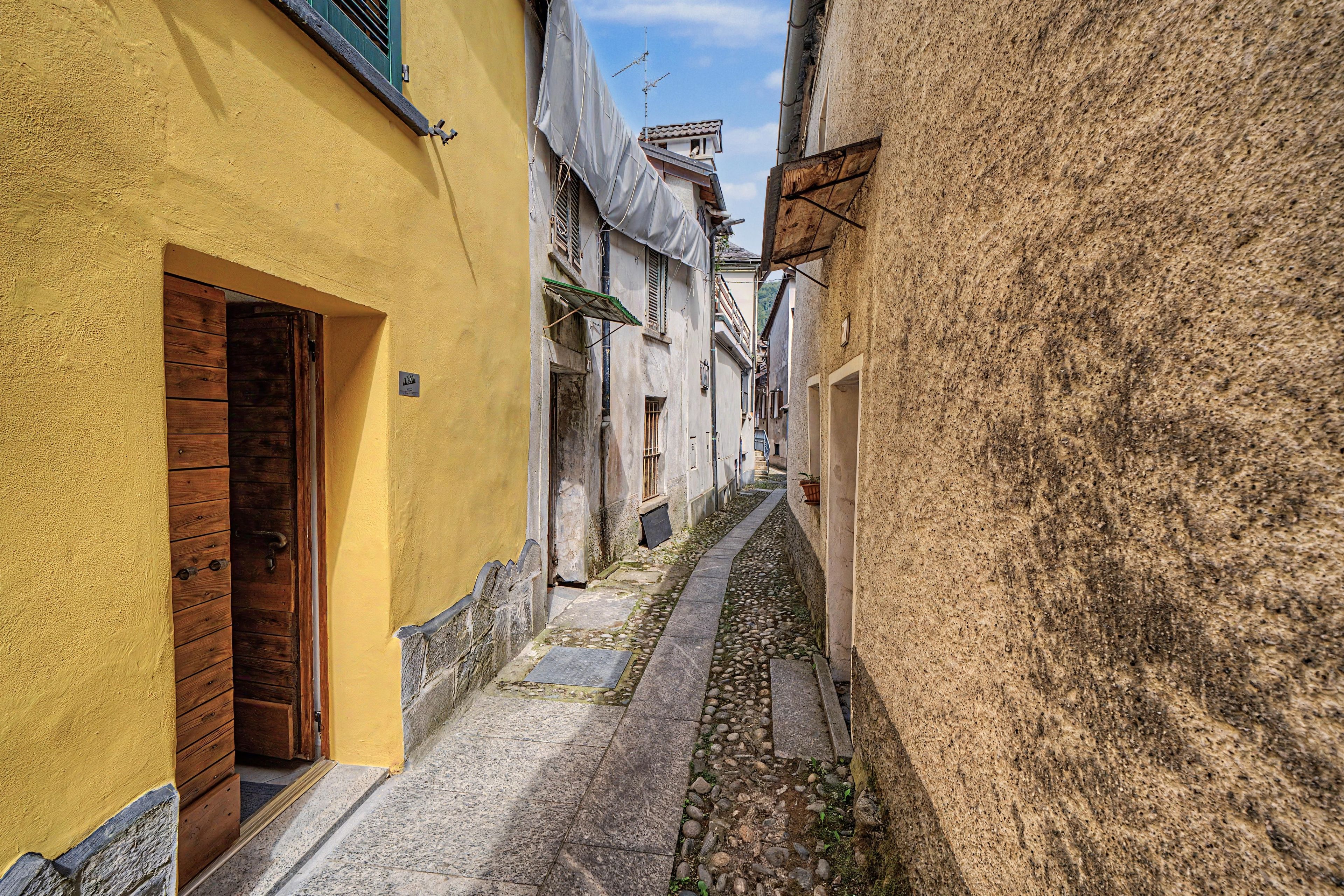 Un estrecho callejón flanqueado por edificios, con una puerta de madera a la izquierda y un sendero de piedra.