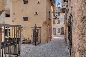 Un carrer empedrat i estret amb edificis històrics, una entrada tancada per una reixa i un cartell de 'Leonardo D'oro'.