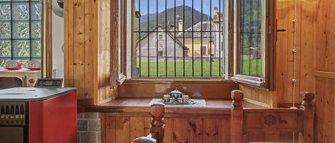 Interior de una cabaña de madera con cocina, una mesa de comedor con mantel a cuadros y una ventana con vistas a un paisaje rural.