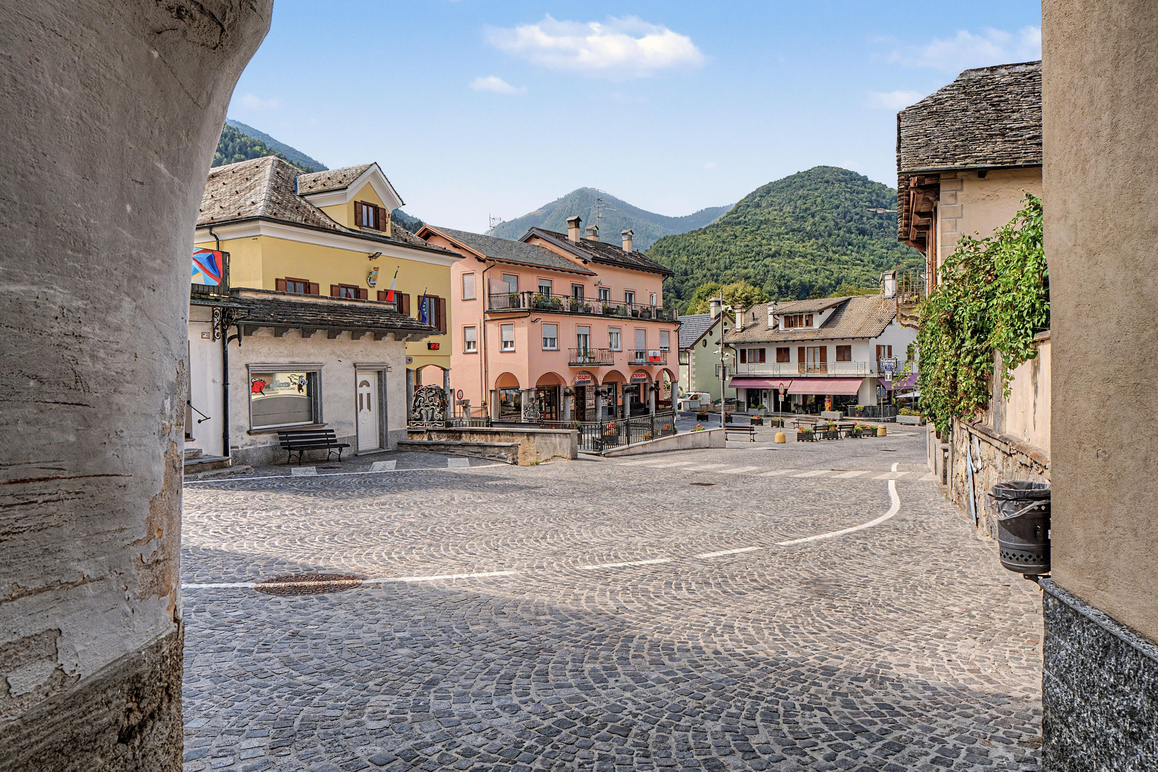 Eine Kopfsteinpflasterstraße in einer historischen Stadt mit traditioneller Bebauung, einem zentralen Platz und einem Berg im Hintergrund.