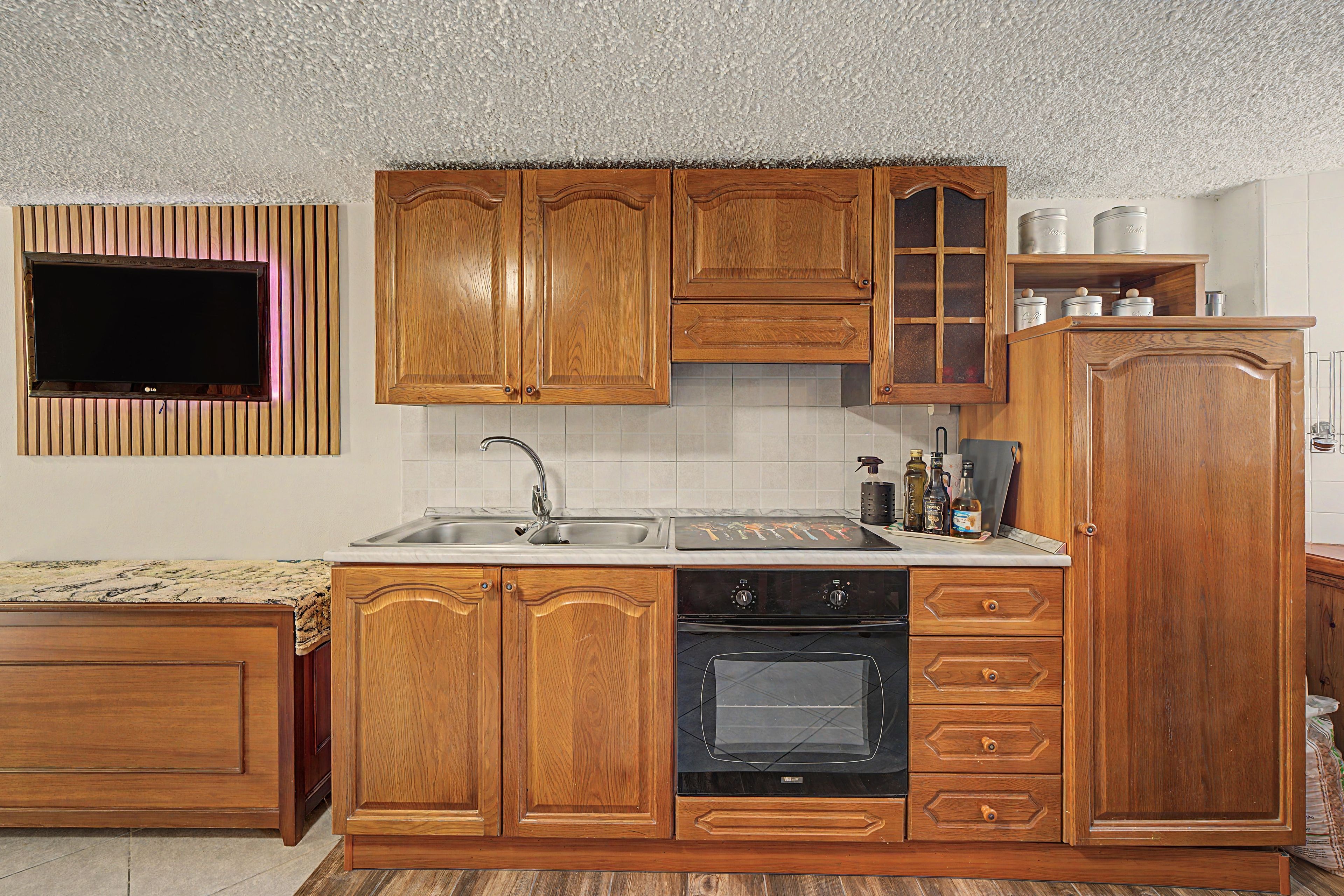 A kitchen with wooden cabinets, a built-in oven, a sink, and a television mounted on the wall.