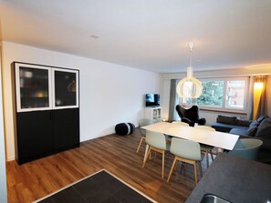 Ein modernes Wohnzimmer mit Essbereich, einer Couch, einem Fernseher und einem großen Fenster.