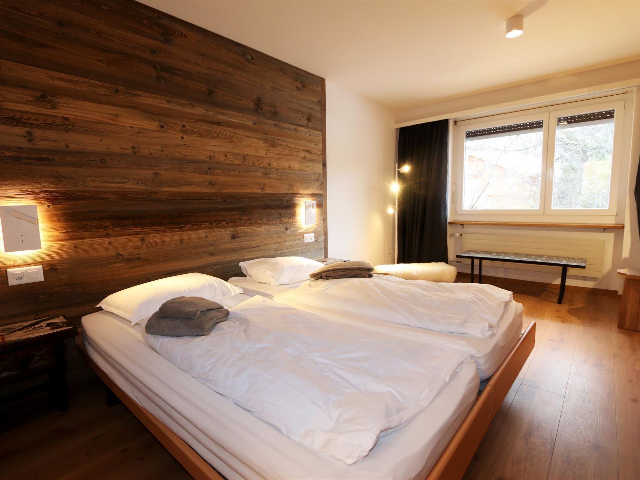 Un lit double avec du linge de lit blanc, une tête de lit en bois, des lampes de chevet et une fenêtre avec des rideaux.