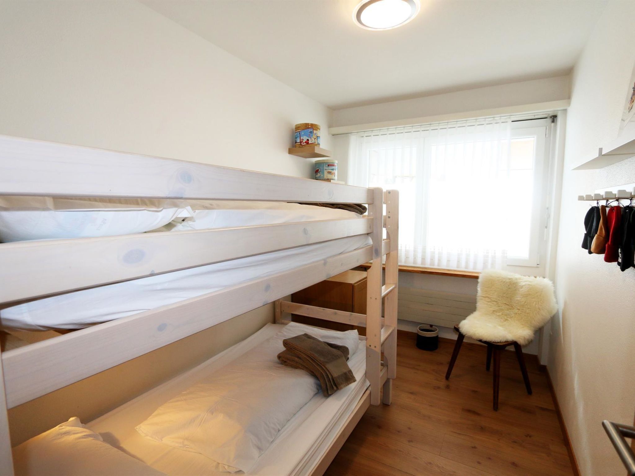 Ett rum med en våningssäng, ett fönster, en stol och en hylla med diverse föremål.