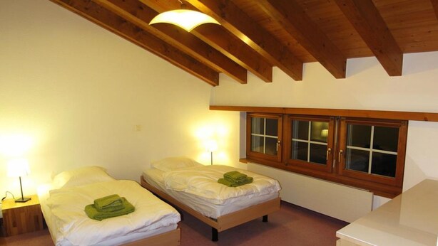 A room with two single beds, a wooden bench, a desk, and a window with curtains. - Flamingo Appartement/Fewo, Dusche und Bad, WC, 4 oder mehr Schlafräume by Interhome (Saas-Fee)