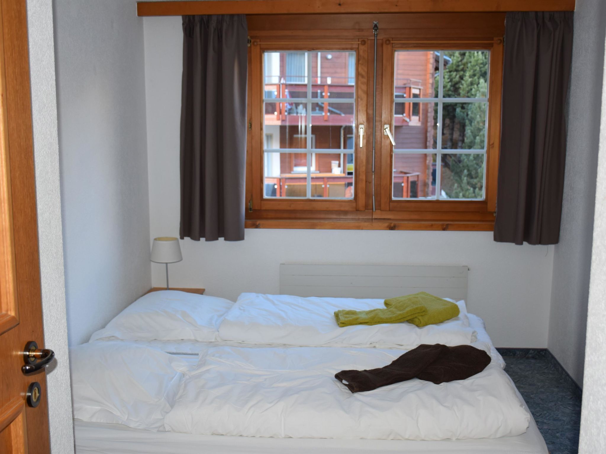 A single bed with white bedding, a lamp, and a window with curtains.