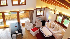 A spacious living area with a high ceiling, wooden beams, a dining table with chairs, a sofa, and a window with curtains. - Flamingo Appartement/Fewo, Dusche und Bad, WC, 4 oder mehr Schlafräume by Interhome (Saas-Fee)