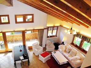 Ein großzügiger Wohnbereich mit hoher Decke, Holzbalken, einem Esstisch mit Stühlen, einer Couch und einem Fenster mit Vorhängen.