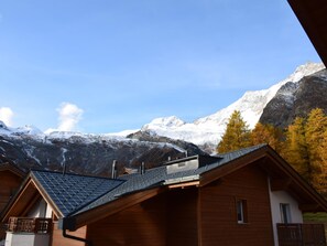 Eine Holzhütte mit geneigtem Dach vor einer Kulisse schneebedeckter Berge und wolkenlosen, blauen Himmel.