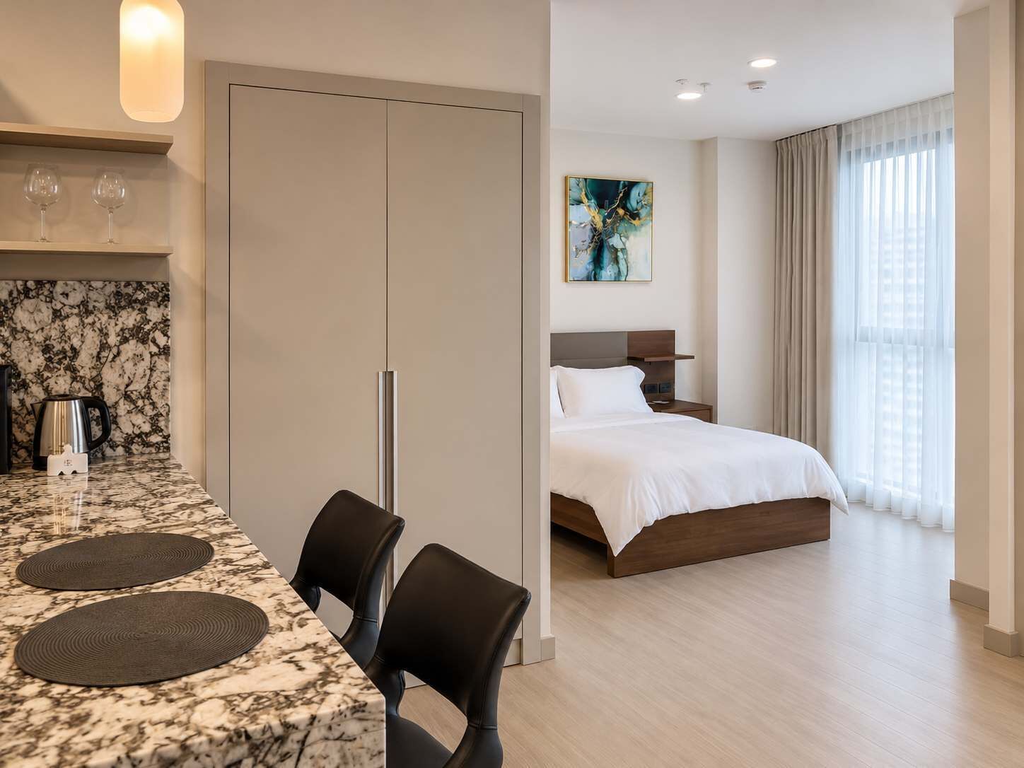 A hotel room with a bed, bedside table, and a view of the city through large windows.