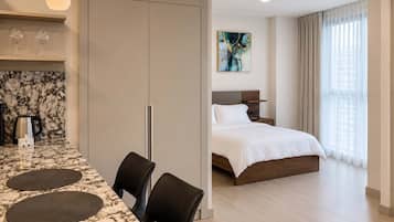 A hotel room with a bed, bedside table, and a view of the city through large windows.