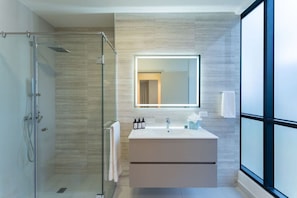Et moderne badeværelse med brusekabine i glas, et stort spejl og et toiletbord med vask.