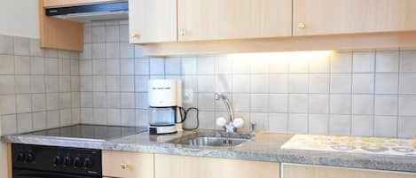 A kitchen with wooden cabinets, a stove, a coffee maker, and a tiled backsplash.