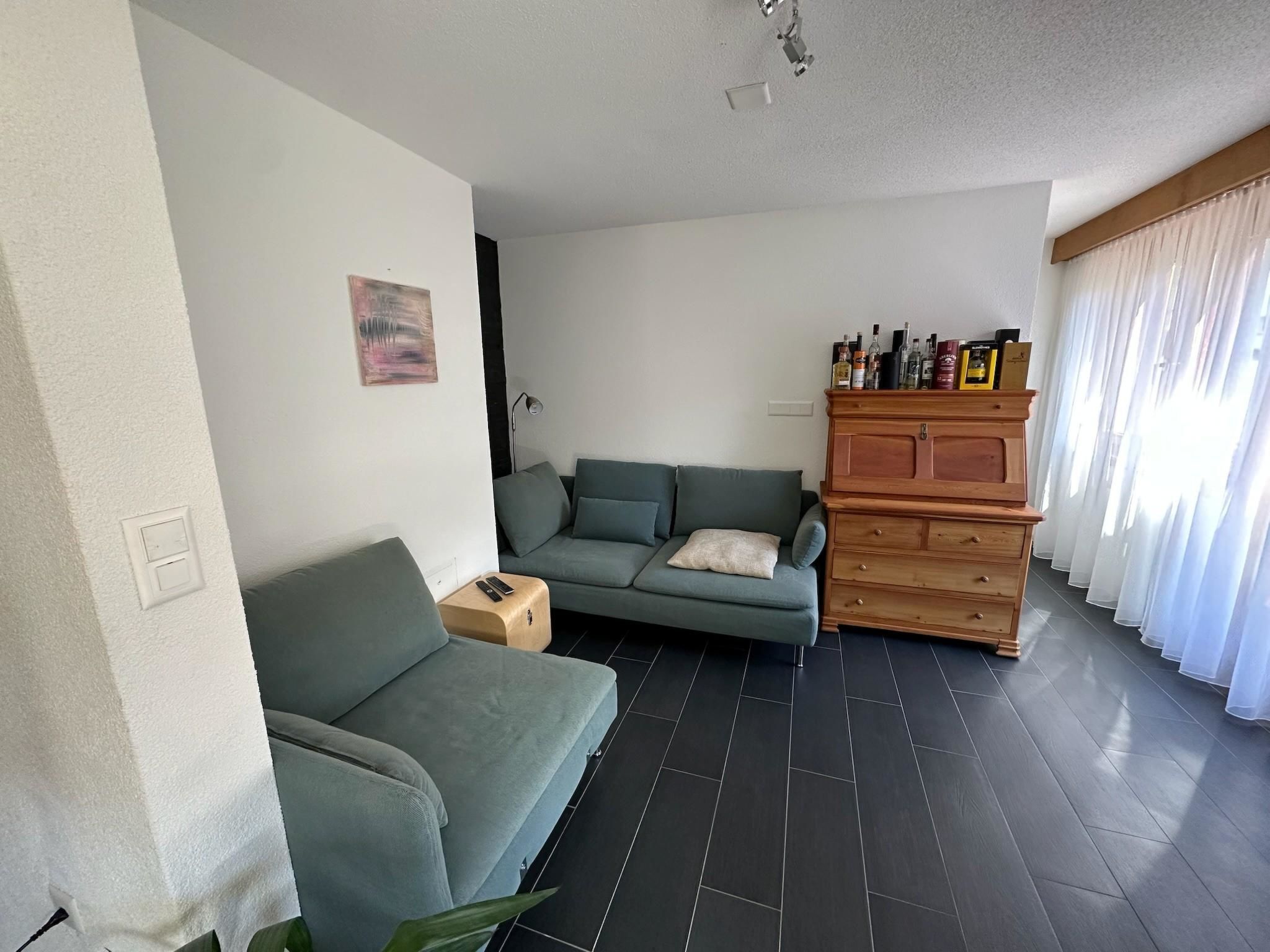 Un salon moderne avec un canapé gris, un meuble en bois contenant des bouteilles et un tableau accroché au mur.