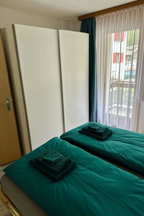 A hotel room with two single beds, a wardrobe, and a window with curtains. - Alouette Appartement/Fewo Apartment Lama by Interhome (Saas-Almagell)