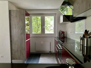 Eine moderne Küche mit Einbauofen, Mikrowelle und Arbeitsplatte aus Edelstahl. Zwei Fenster sorgen für natürliches Licht und bieten einen Blick ins Grüne.