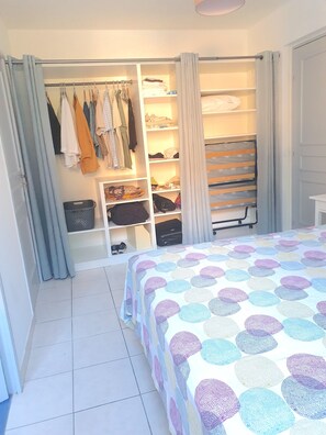Ein Schlafzimmer mit einem Bett, einem Schrank mit Kleidung und einem Regal mit gefalteten Gegenständen.