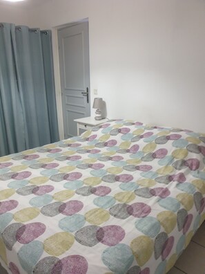 A bedroom with a bed, a nightstand, a lamp, and a door. - Apartment near the beach (Menton)