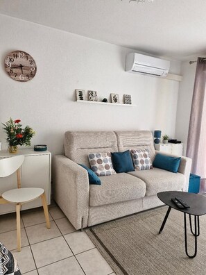 Ein modernes Wohnzimmer mit Sofa, Beistelltisch, Sessel, Couchtisch und Wanduhr.