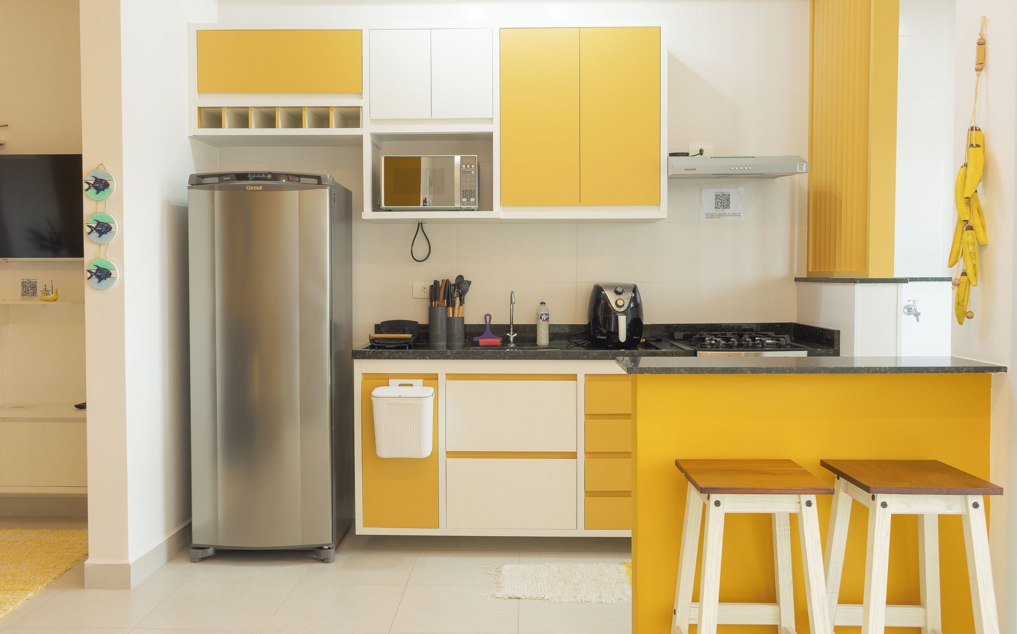 A kitchen with a stainless steel refrigerator, microwave, and stove, with yellow cabinets and a small island with stools.