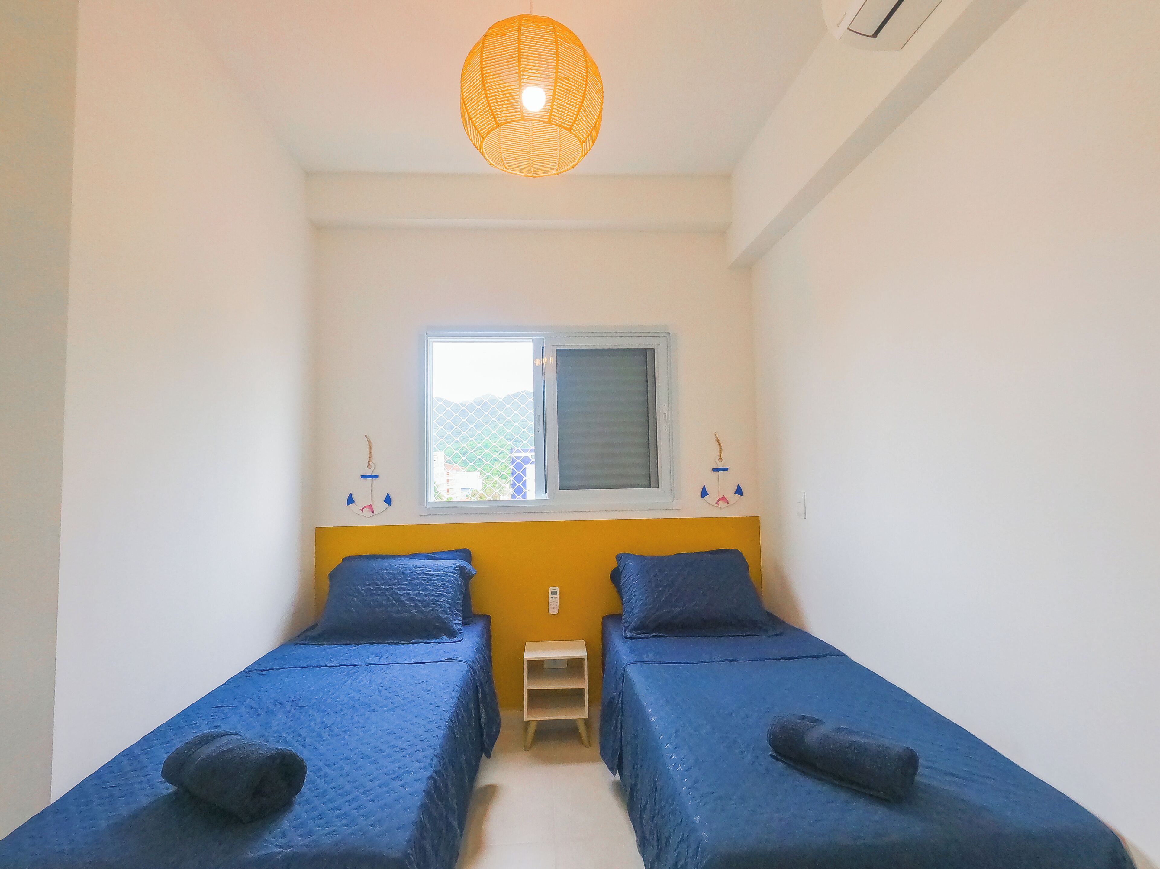 Ein kleines Zimmer mit zwei Betten, einem Fenster und einer Hängelampe.