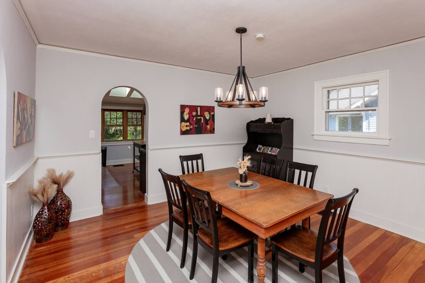 Uma sala de jantar com uma mesa de madeira, seis cadeiras, um candelabro e um piano.