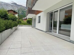 A modern building with a paved walkway, large sliding glass doors, and a view of mountains in the background. - Romaine Appartement/Fewo Appartement/Fewo by Interhome (Saas-Fee)