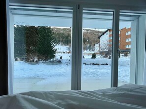 Ein Zimmer mit großem Fenster und Blick auf eine verschneite Landschaft mit Gebäuden und Bäumen.