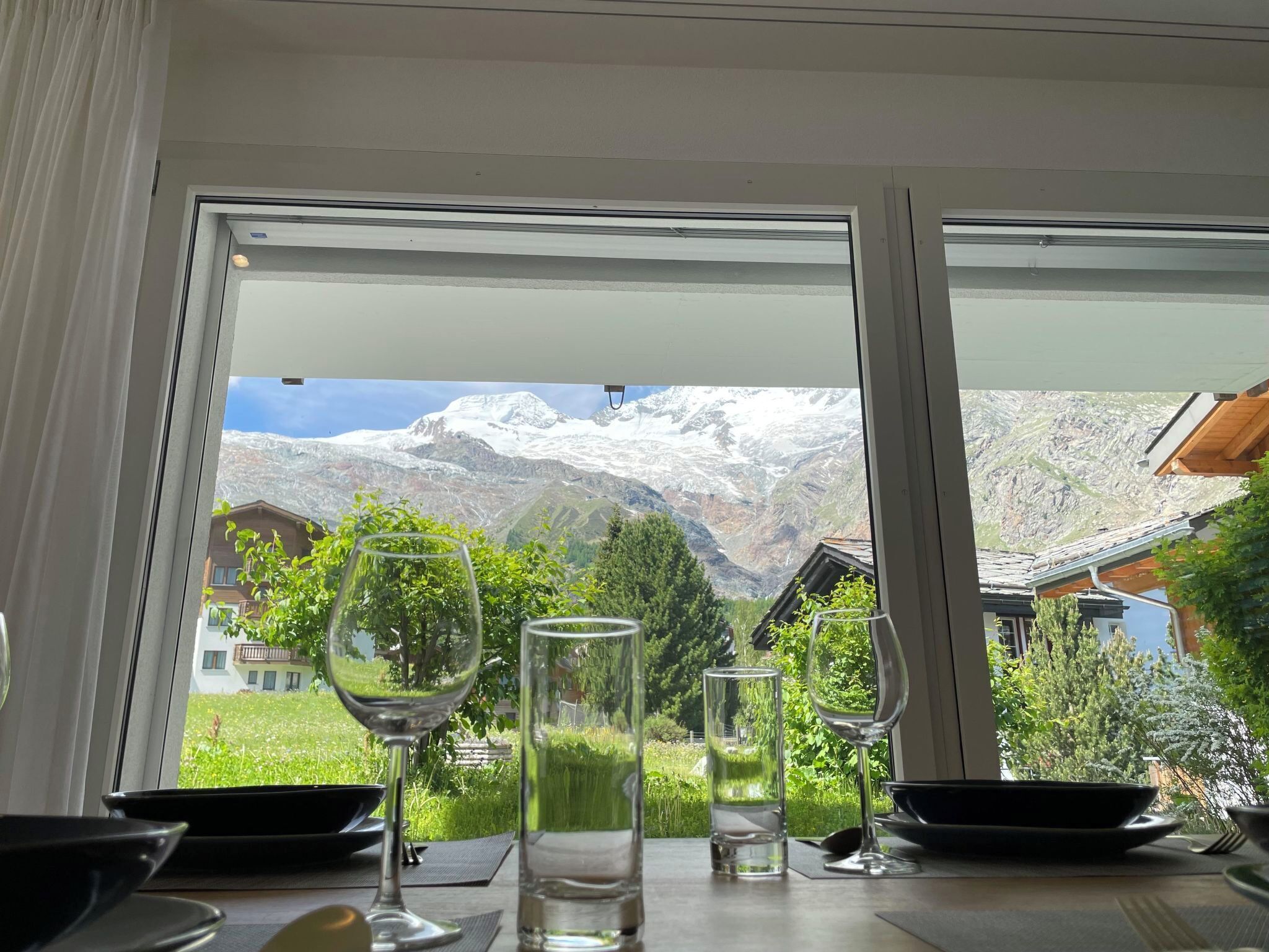 A dining table with wine glasses and a bowl, set against a window with a mountain view.