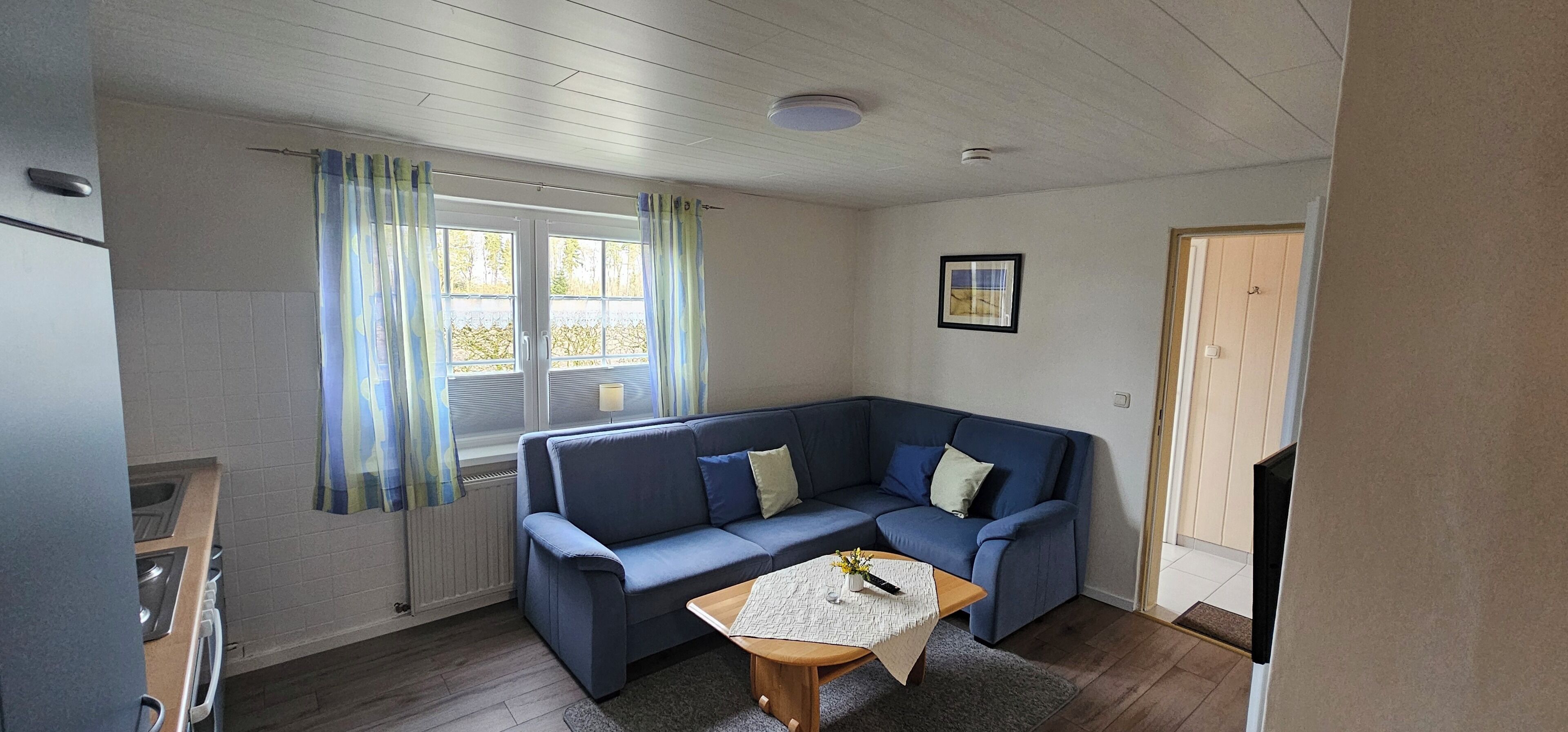 A small, cozy room with a blue sofa, a wooden table, and a window with curtains.