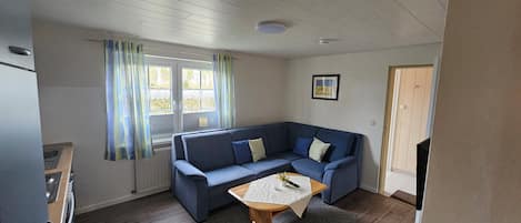 Una habitación pequeña y acogedora con un sofá azul, una mesa de madera y una ventana con cortinas.