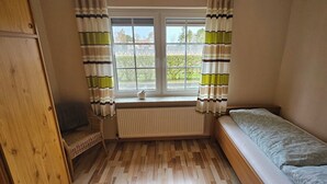 Um quarto pequeno com janela, radiador, cama e guarda-roupa de madeira.