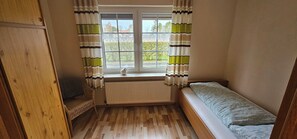 A small room with a window, a radiator, a bed, and a wooden wardrobe. - Vacation Rental on the North Sea Coast: Holtgast-Fulkum (Holtgast)