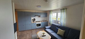 Un espace de vie compact comprenant un coin cuisine, un canapé et une fenêtre avec des rideaux.