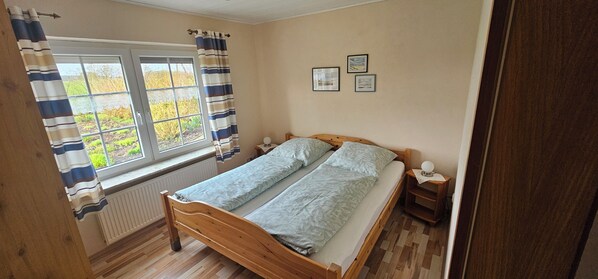 Une chambre à coucher avec un lit en bois, une fenêtre avec des rideaux, un radiateur et deux tables de chevet avec des lampes.