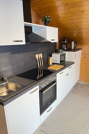 A modern kitchen with white cabinets, a black countertop, stainless steel appliances, and a wooden ceiling. - Allalinblick Appartement/Fewo 4. OG Bergseite by Interhome (Saas-Grund)