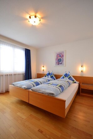 Ein Schlafzimmer mit einem Holzbett, zwei Nachttischen, einem Fenster mit Vorhängen und einer Wandleuchte.