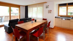 A modern kitchen with a wooden countertop and built-in appliances, a dining area with a wooden table and red chairs, and a large window with curtains. - Aramis Appartement/Fewo 6-Bettwohnung Nr. 2 by Interhome (Saas-Fee)