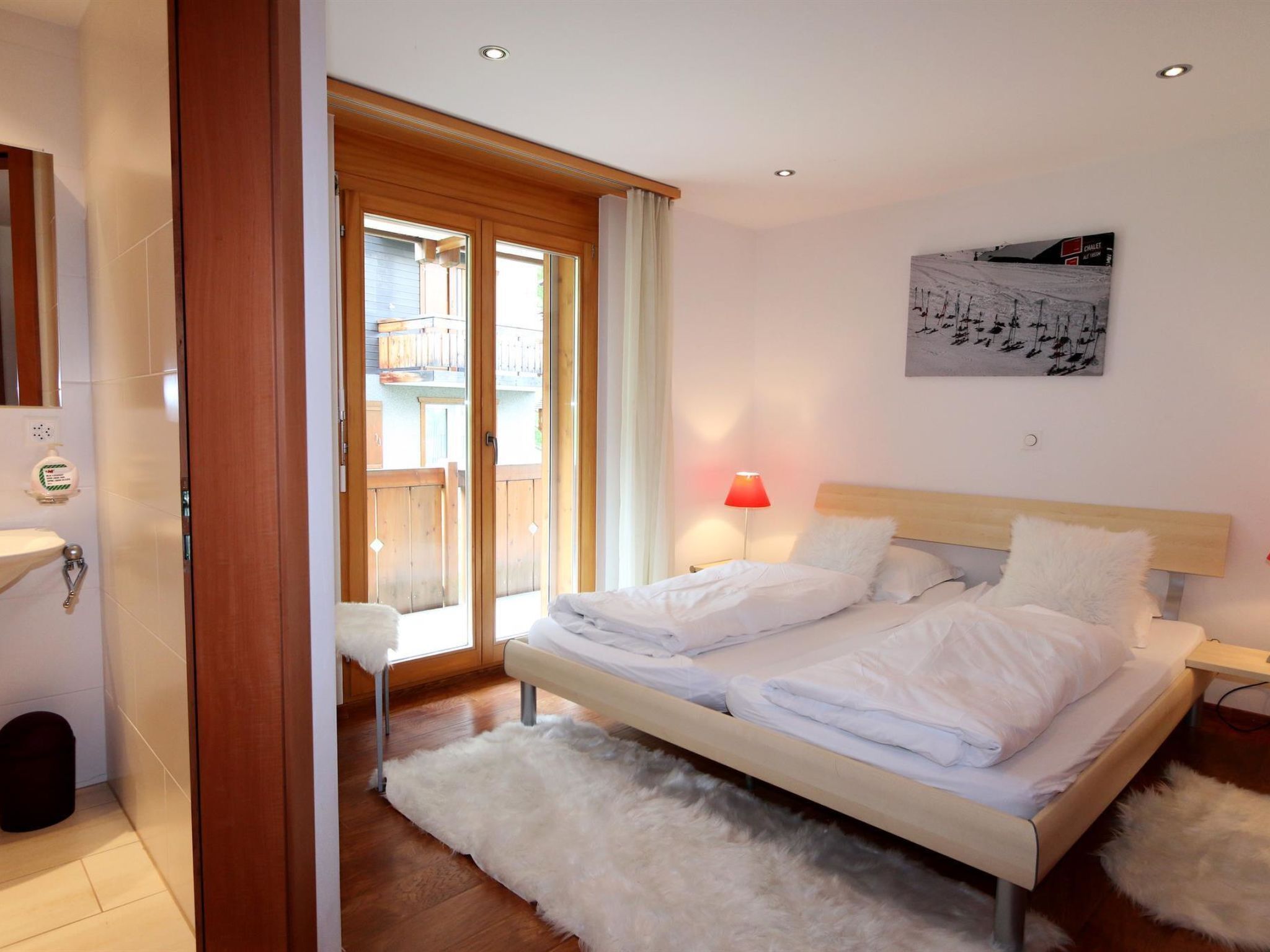 Ein Schlafzimmer mit einem Bett, einem Nachttisch, einem Fenster mit Vorhängen, einem Wandbild und einer Holztür.