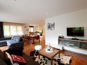 Una sala de estar moderna con sofá, comedor, cocina y televisor montado.