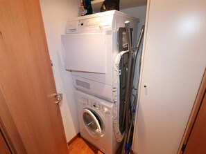 Un lavadero pequeño con electrodomésticos apilados, que incluye una secadora, lavadora y plancha.