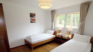 Quarto de hotel com duas camas de solteiro, piso de madeira, um quadro na parede e uma janela com cortinas.