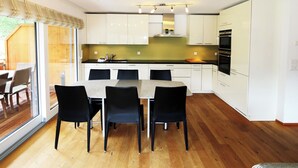 Uma cozinha moderna com armários brancos, uma mesa de jantar com cadeiras e vista para o exterior através de uma porta deslizante.