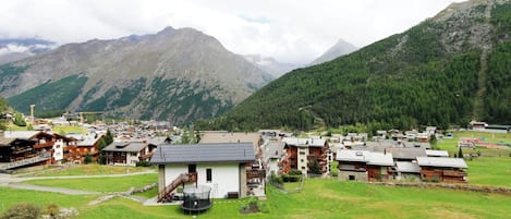 Un pueblo montañoso con casas de madera tradicionales, un edificio central de color blanco con balcón, y una vista despejada de los picos circundantes.