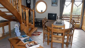 Un comedor con una mesa redonda, sillas de madera, un televisor y una escalera con barandillas de madera.