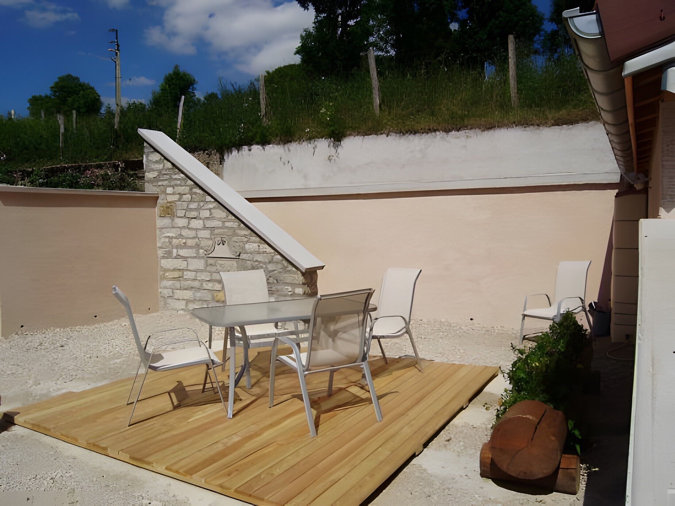 Un patio al aire libre con una mesa y sillas, un muro de piedra y una terraza de madera.