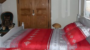 Un dormitorio con un armario de madera, una cama con ropa de cama roja y blanca, y un oso de peluche en una silla.