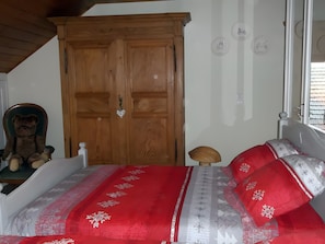 Ein Schlafzimmer mit einem Holzschrank, einem Bett mit rot-weißer Bettwäsche und einem Teddybären auf einem Stuhl.