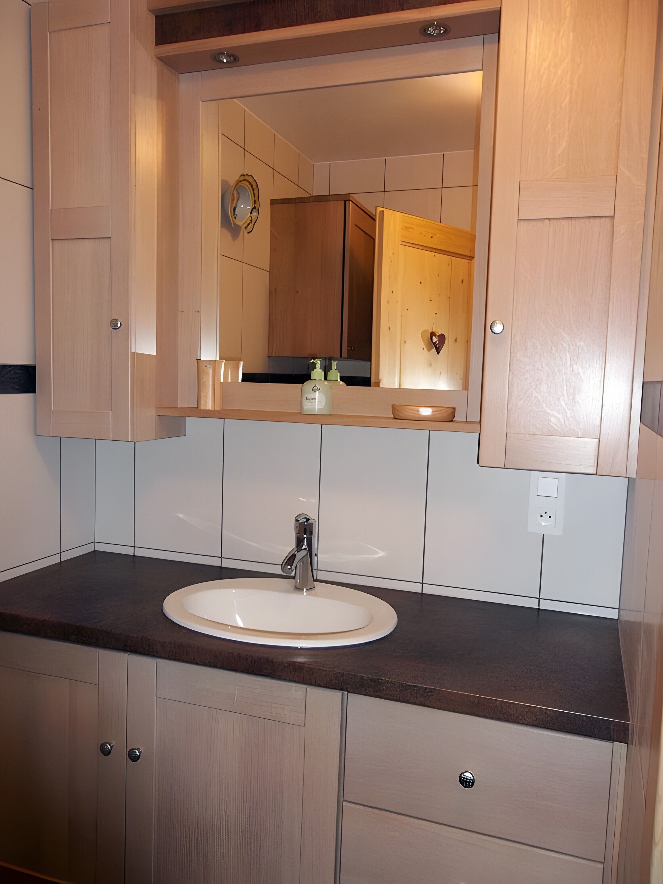 Un bany amb un lavabo blanc, armaris de fusta i un mirall sobre el lavabo.