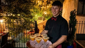 A person holding a tray with six glasses of a beverage, possibly cocktails, in an outdoor setting with a fence and greenery in the background. - Stone-Walled 1-Bed with Fireplace · Sleeps 2 by St Edward`s Church, Castle Donington (Castle Donington)